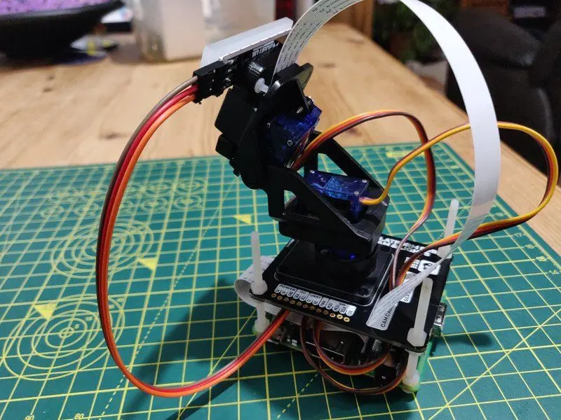 Top view of the assembled unit sitting upright. The Pan-Tilt HAT is mounted on the Pi with a camera extending from the HAT. Wires lead from all side up to the camera and a LED light.