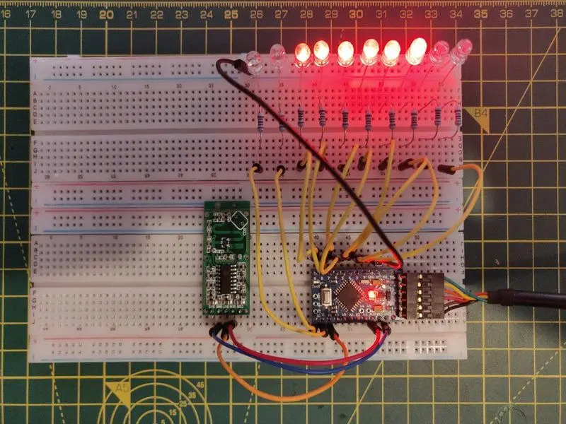 Two breadboards, the top one has all of the LEDs slotted in and they are lit up red. The bottom one has the Arduino and a PIR motion detector. Wires connect the two boards.