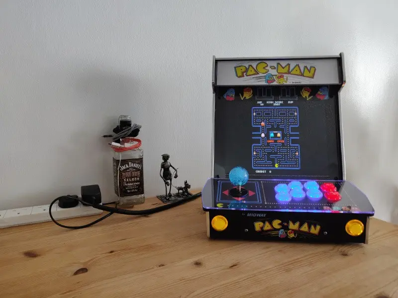 The completed cabinet shown from the front, all buttons illuminated and Pac-Man playing on the display.