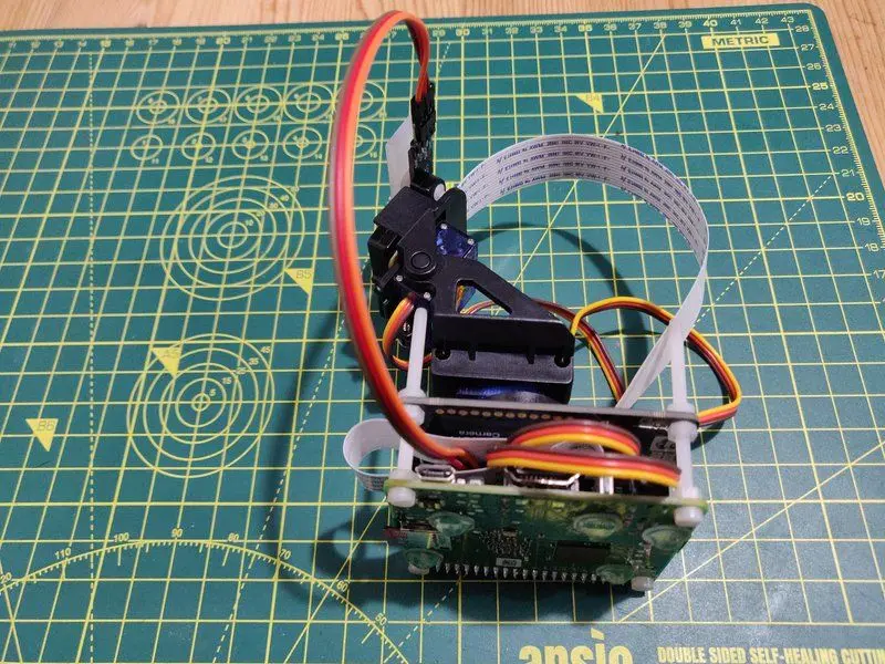 Side view of a Raspberry Pi 3A connected to a Pimoroni Pan-Tilt HAT which has a camera connect to it. The Pi has long nylon screws coming out of it. It is fully assembled. This will become the head of the robot CCTV unit